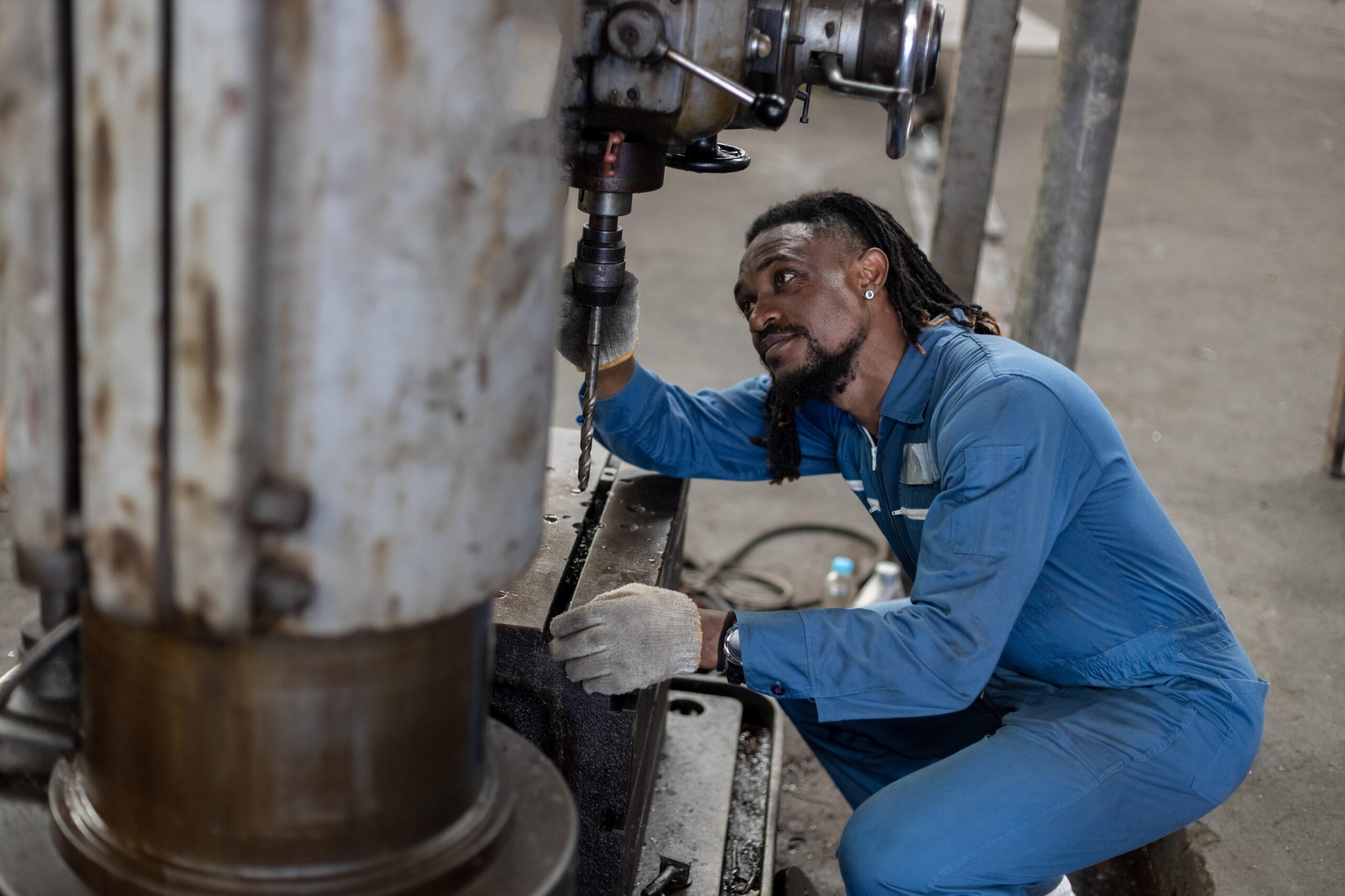 Male african american workers wear yellow hard hat working on repairing factory machinery. Man maintenance electric drill of factory. Mechanical repairman concept.