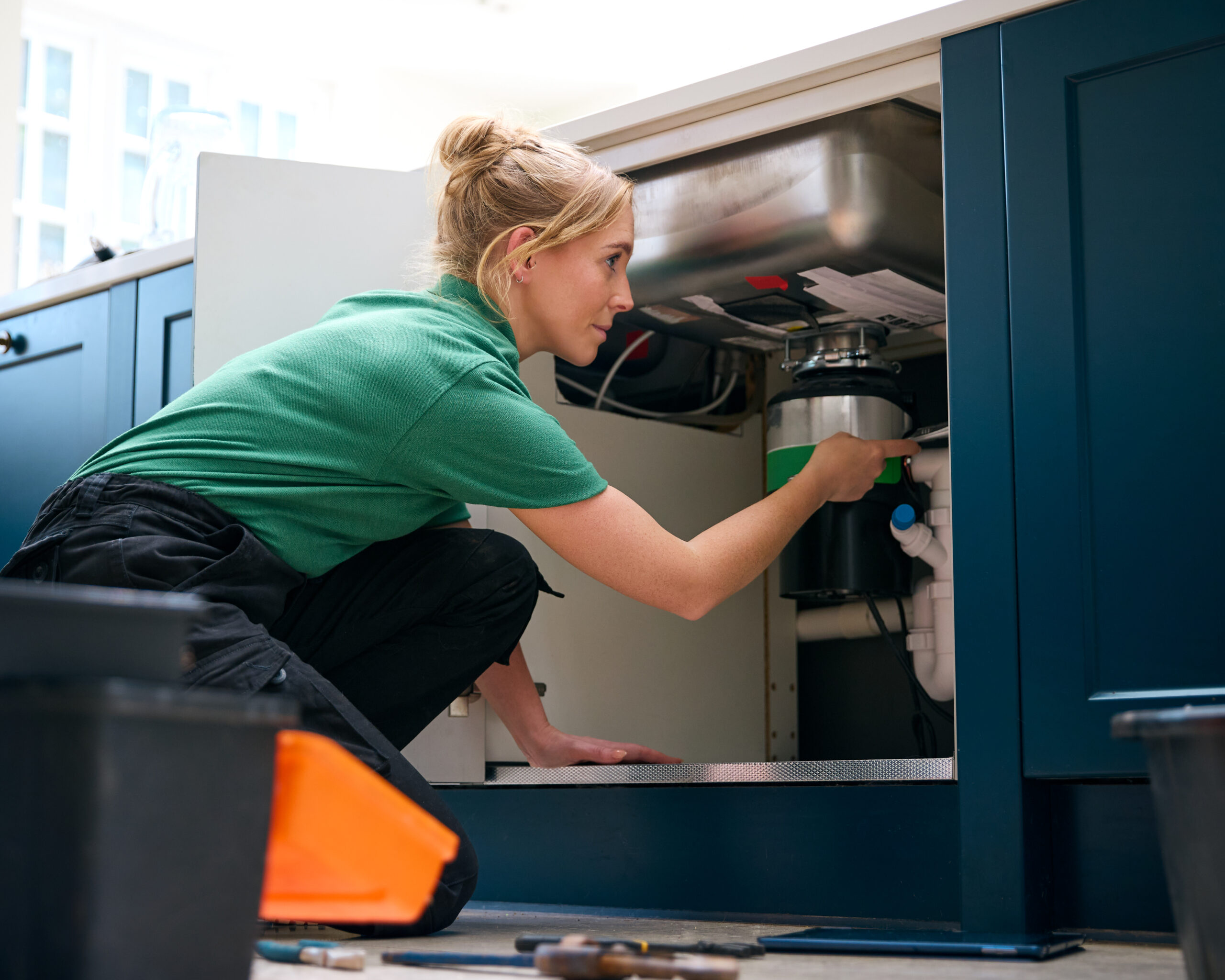 Female Plumber With Digital Tablet Fixing Waste Disposal Unit In Domestic Kitchen Sink